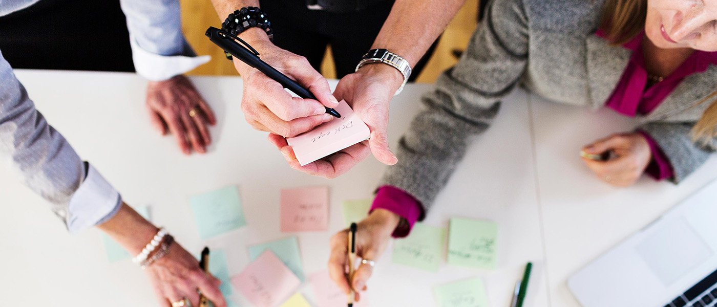 Three persons writing on post its