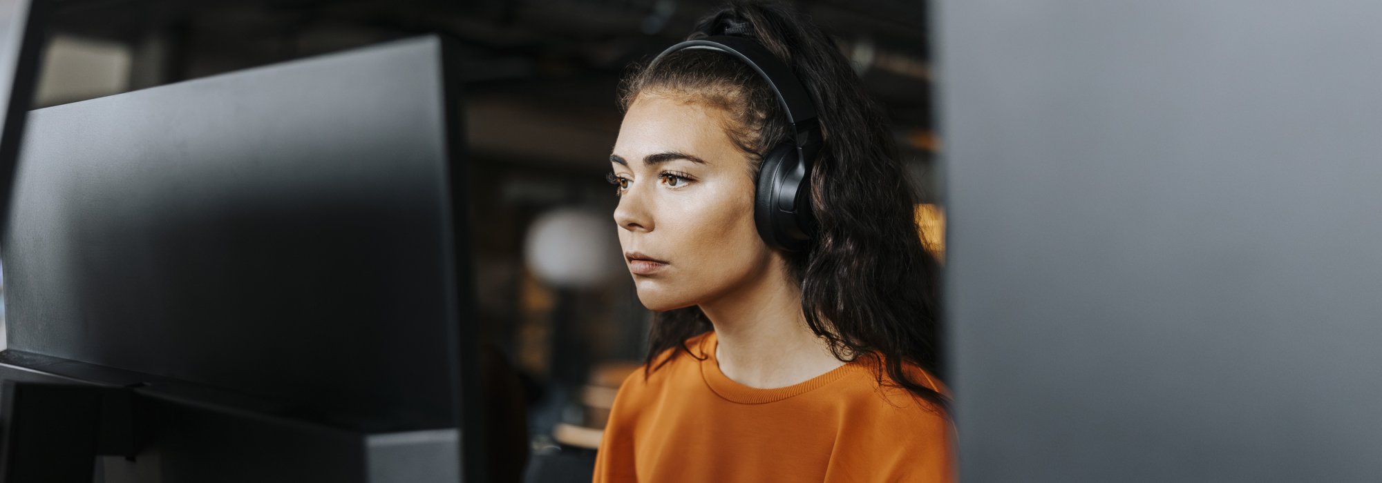 A woman working at a computer wearing wireless headphones