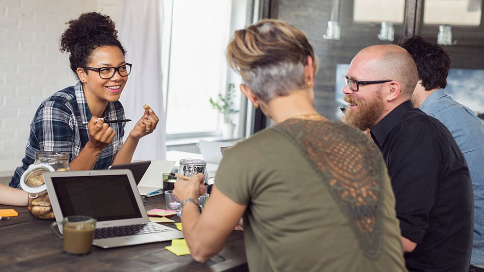 Three colleagues sitting around a table discussing smiling