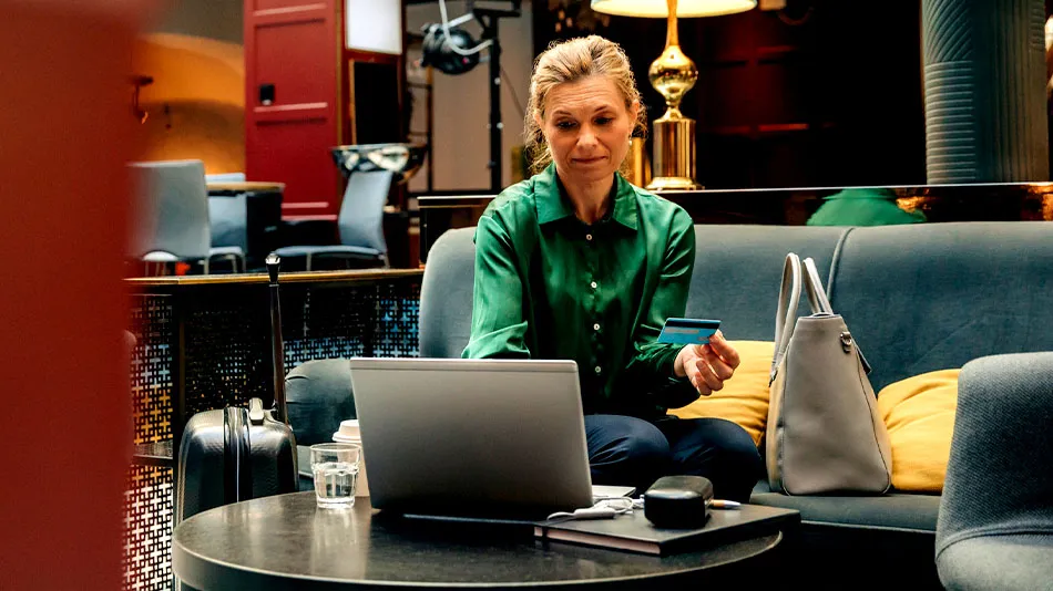 Mature businesswoman holding credit card while using laptop sitting in hotel lounge.