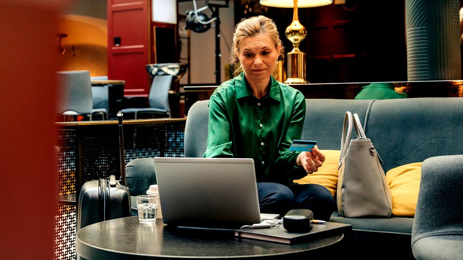 Mature businesswoman holding credit card while using laptop sitting in hotel lounge.