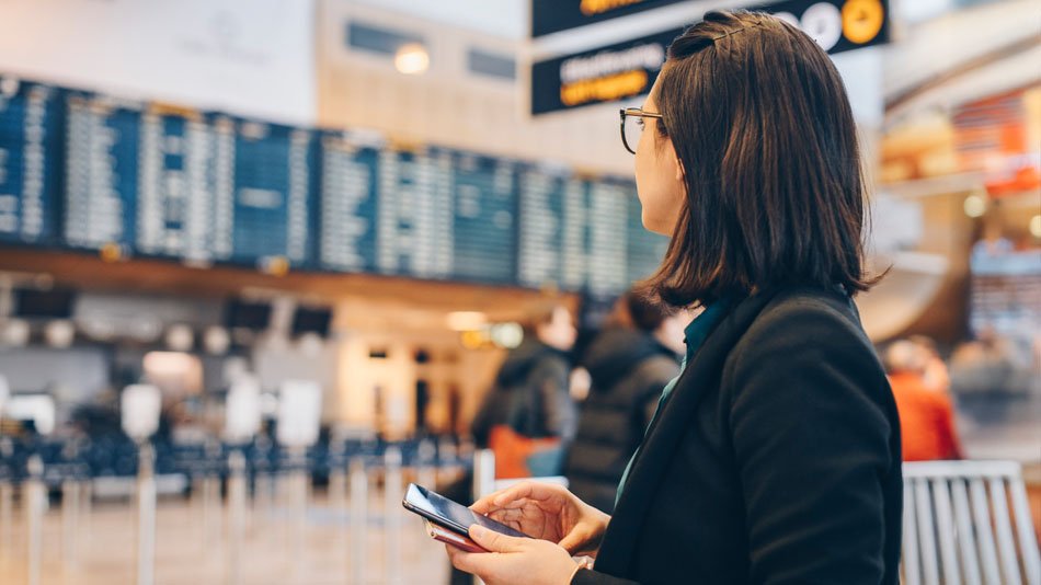  Mid adult businesswoman holding mobile phone while standing in airport