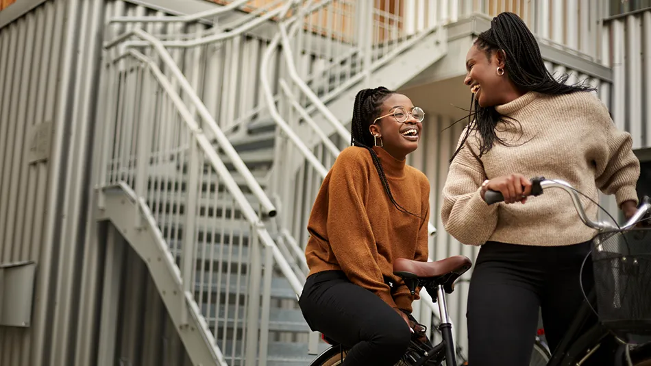 Two women riding a bike during the day, they are laughing