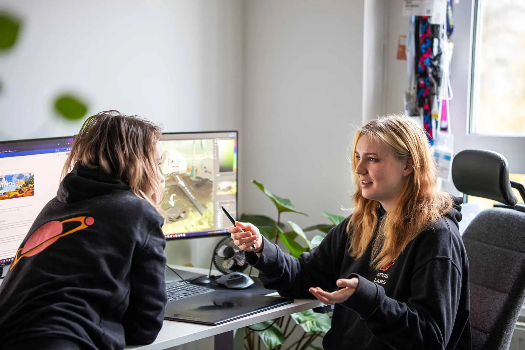 Two female colleagues discussing, monitors in the background